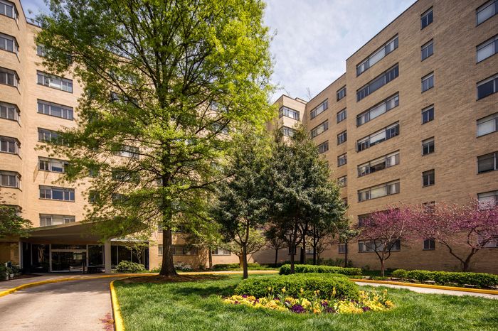 Elegant apartment complex with lush landscaped gardens, mature trees, and vibrant flowerbeds, offering tranquil urban living.