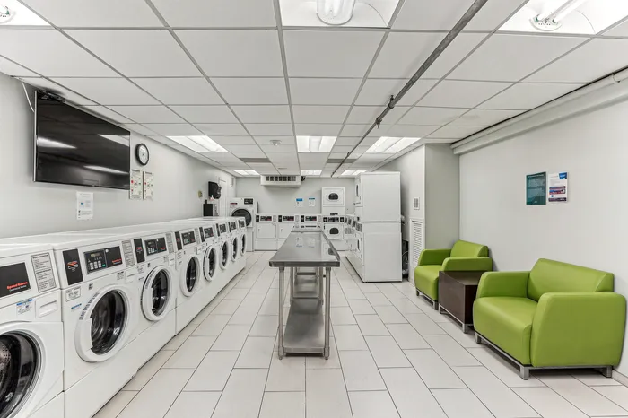 Modern laundry room with multiple washing and drying machines, comfortable seating area, and sleek design.