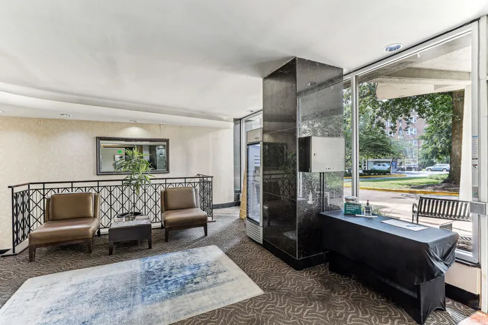 Chic apartment lobby with stylish seating, elegant mirror, and floor-to-ceiling windows offering a lovely street view.