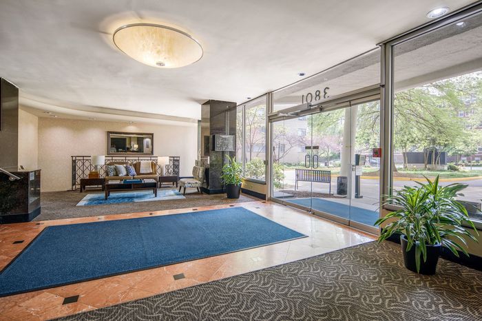 Elegant apartment lobby with stylish seating area, lush indoor plants, and large glass doors opening to a vibrant outdoor view.