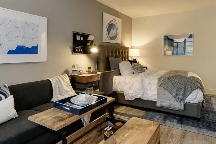 Chic studio apartment showcasing a cozy bedroom with a plush bed, stylish sofa, and modern workspace in a warmly lit setting.