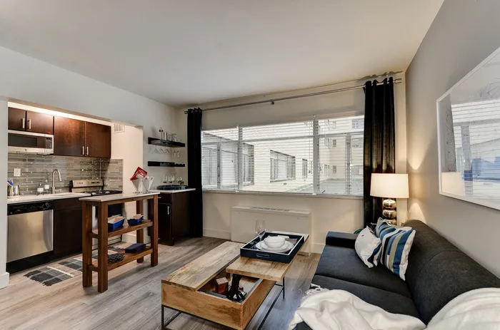 Modern open-plan living room and kitchen with stylish furnishings, large window, and sleek wooden accents.
