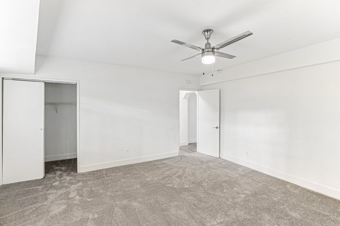 Bright, spacious apartment bedroom with plush carpeting, modern ceiling fan, and ample closet space.