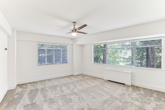 Bright and spacious room with large windows, fresh carpeting, and stylish ceiling fan, perfect for comfortable modern living.