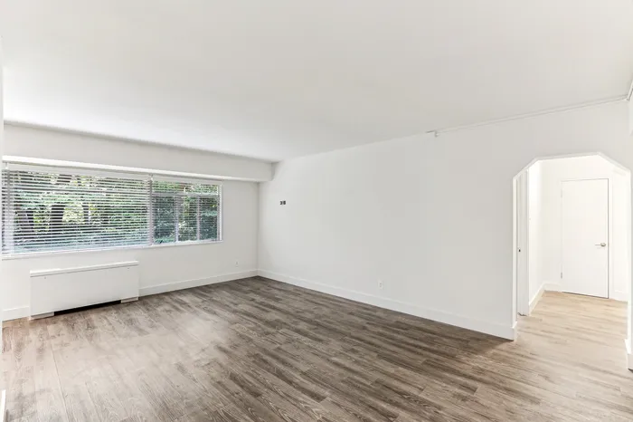 Bright and spacious living room featuring large windows with lush green views and elegant hardwood flooring.