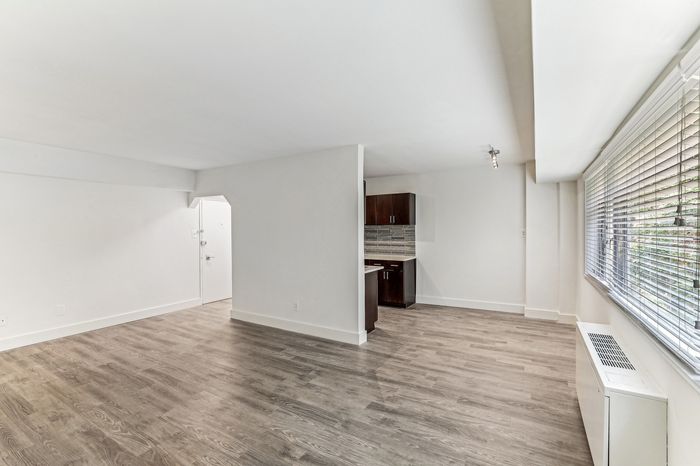Bright and spacious living area with elegant wood flooring, modern kitchen nook, and large windows providing ample natural light.
