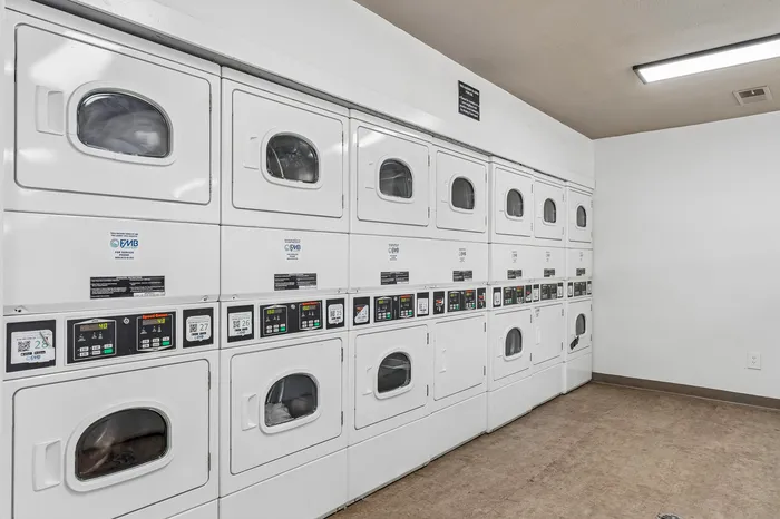 Modern communal laundry room featuring rows of easy-to-use dryers and washers, perfect for convenient apartment living.