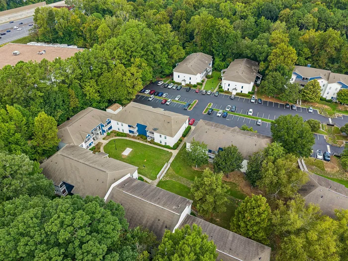 Charming aerial view of a serene apartment complex nestled among lush greenery with spacious parking and easy highway access.