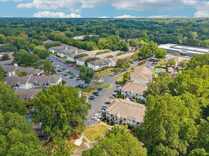 Charming aerial view of a lush residential community surrounded by greenery, showcasing modern apartments with ample parking and recreational spaces.