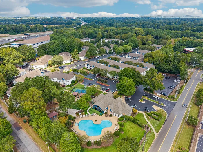 Aerial view of lush apartment complex surrounded by greenery, featuring a stunning central pool and inviting pathways, ideal for serene living.