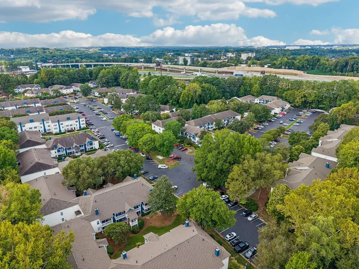 Scenic aerial view of a charming apartment community nestled amidst lush greenery, showcasing convenient parking and well-maintained living spaces.