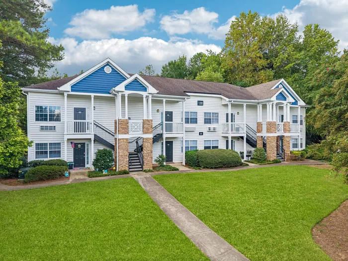 Charming apartment complex with modern two-story design, highlighted by elegant white siding and inviting balconies, set amidst lush greenery and a well-maintained lawn.