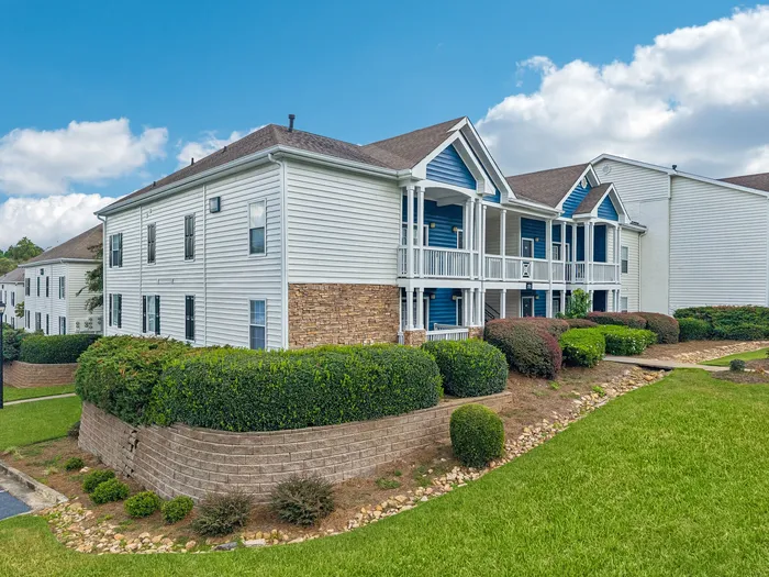 Charming white and blue apartment buildings with manicured landscaping under a bright blue sky.