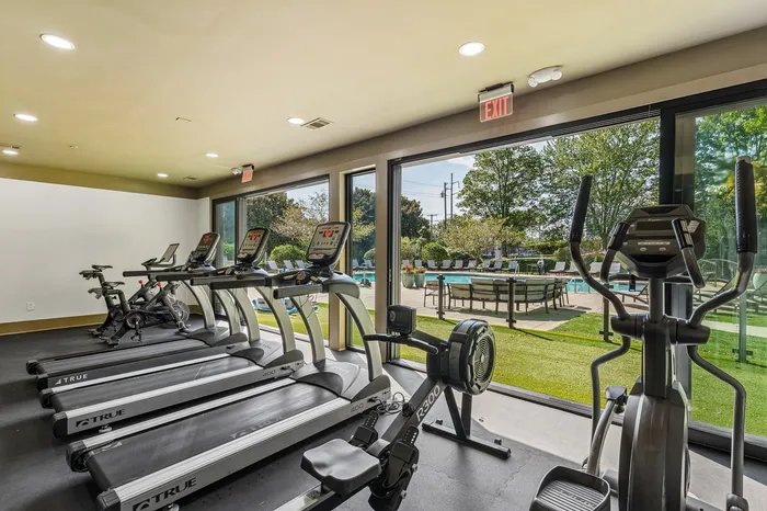 Modern fitness center with state-of-the-art equipment and scenic outdoor pool view through floor-to-ceiling windows.