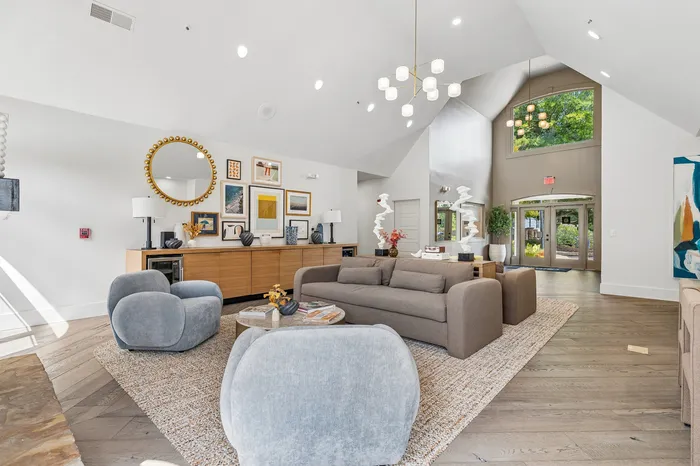 Spacious modern living room with vaulted ceiling, elegant chandelier, and stylish decor featuring soft gray seating and artistic wall gallery.
