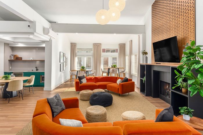 Chic open-concept living area featuring vibrant orange sofas, modern kitchen with green cabinetry, and abundant natural light.