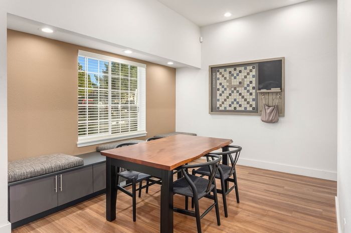 Inviting dining area with a stylish wooden table, chic black chairs, large window bringing natural light, and modern decor on hardwood flooring.
