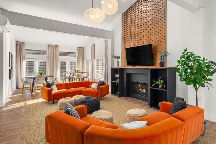 Modern living room featuring vibrant orange sofas, a stylish wood-paneled fireplace, and abundant natural light through large windows.