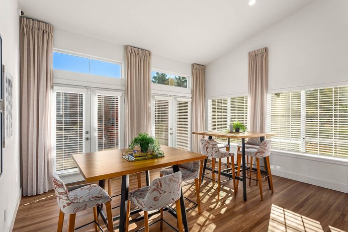 Bright and inviting dining area with stylish high tables and chairs, surrounded by floor-to-ceiling windows with elegant curtains, offering abundant natural light.