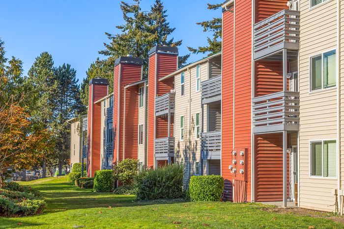 Charming apartment complex with vibrant red and beige exteriors, nestled in lush greenery and surrounded by tall trees.