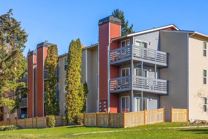Charming apartment exterior with modern balconies, lush greenery, and a vibrant red accent wall.
