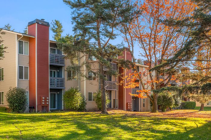 Charming apartment complex nestled among vibrant autumn trees, featuring spacious balconies and lush green surroundings.
