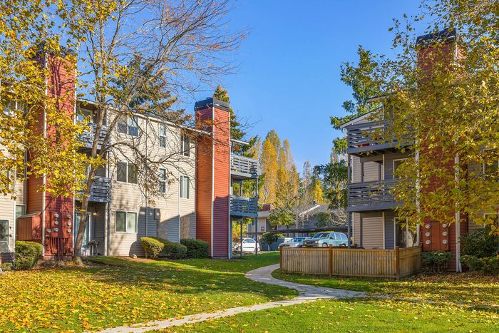 Charming apartment complex nestled among vibrant autumn trees, featuring spacious balconies and a peaceful lawn setting.