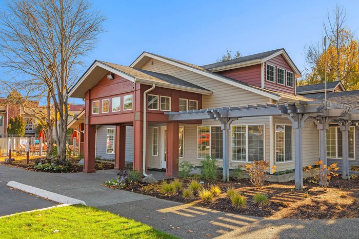 Charming apartment complex with a modern exterior, large windows, and a beautifully landscaped entrance basking in sunlight.