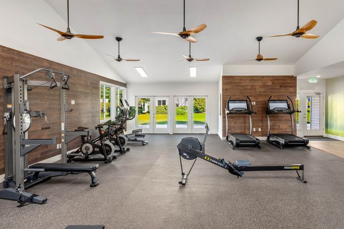 Modern fitness center with state-of-the-art equipment, including treadmills, rowing machines, and exercise bikes, set in a bright and spacious room with wood accents and ceiling fans.
