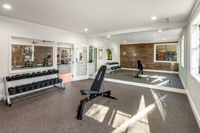 Modern fitness room with mirrored walls, workout bench, and dumbbell rack, offering a bright and inviting exercise space.