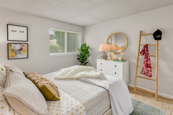 Charming bedroom with plush bedding, modern decor, and natural light through a large window, offering a cozy and inviting retreat.