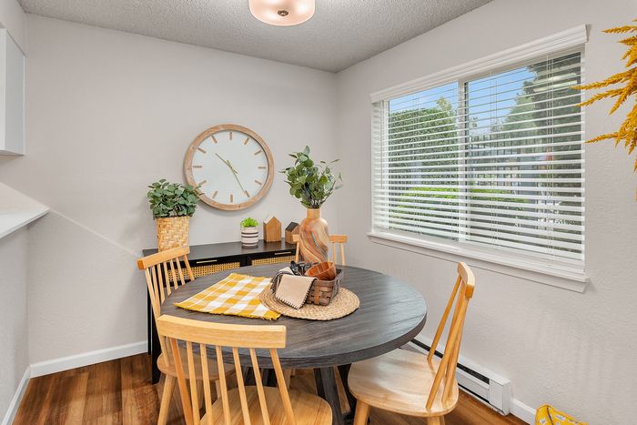 Bright and inviting dining room with a modern round table, wooden chairs, and a large window offering lush greenery views.