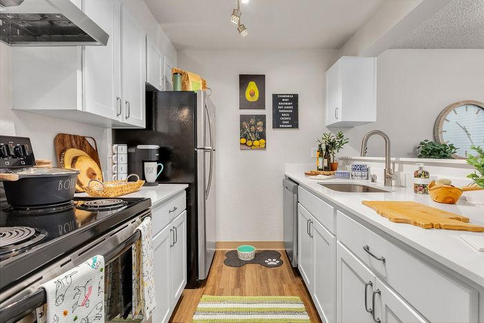 Chic modern kitchen with sleek white cabinets, stainless steel appliances, and warm wood flooring, accented by vibrant wall art and a fresh, inviting atmosphere.