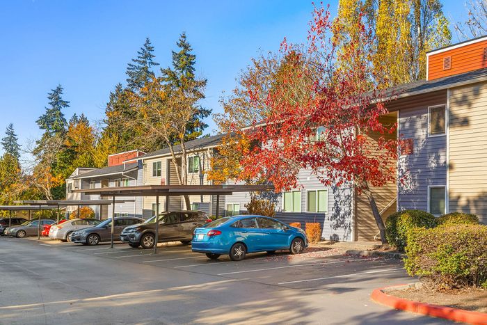 Charming two-story apartment complex with vibrant autumn foliage, covered parking, and serene landscape under a clear blue sky.