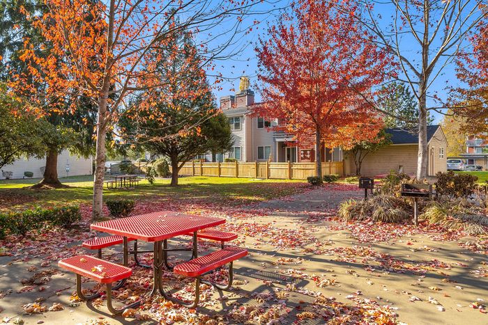 Charming autumn landscape with vibrant red and orange leaves, featuring a cozy outdoor seating area and a nearby apartment building.