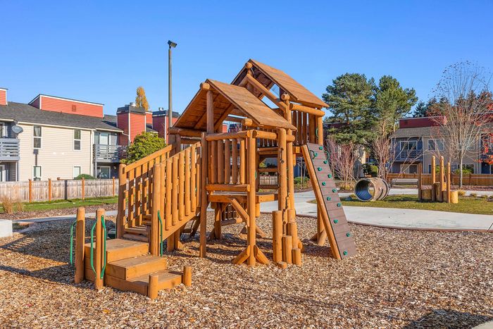 Charming outdoor playground with wooden climbing structure, set against modern apartment buildings, offering family-friendly living.