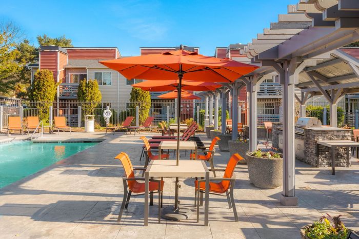 Inviting patio area with vibrant orange umbrellas and modern seating beside a sparkling pool, perfect for outdoor leisure and social gatherings.