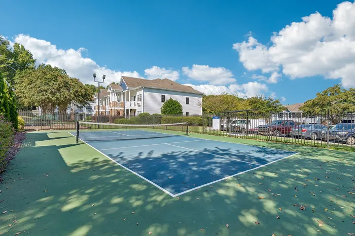 Inviting outdoor tennis court surrounded by lush greenery and charming residential buildings, perfect for an active lifestyle.
