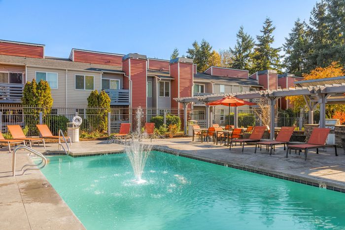 Inviting apartment complex with a sparkling pool, relaxing lounge chairs, and vibrant outdoor seating area under sunny skies.