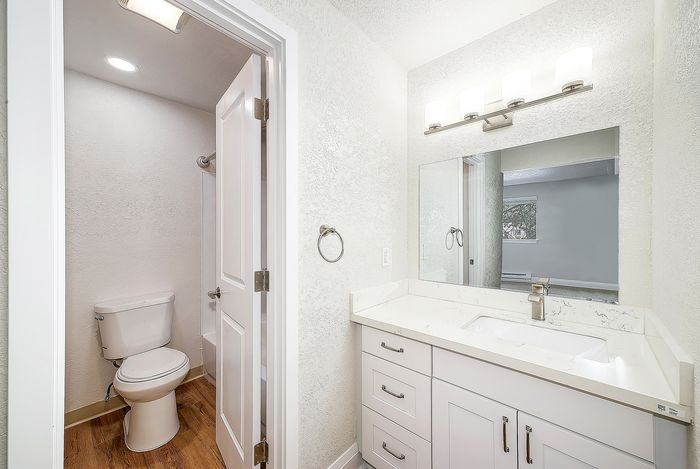 Bright and modern bathroom with elegant white vanity, sleek fixtures, and warm wood flooring.