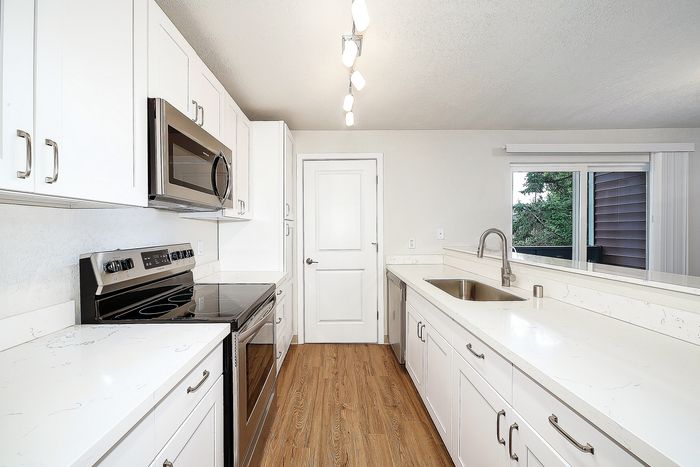 Modern galley kitchen with sleek stainless steel appliances, white cabinetry, and large windows providing ample natural light.