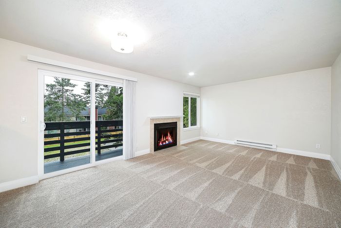 Bright and spacious living room featuring a cozy fireplace, plush carpeting, and a large sliding door opening to a scenic balcony view.