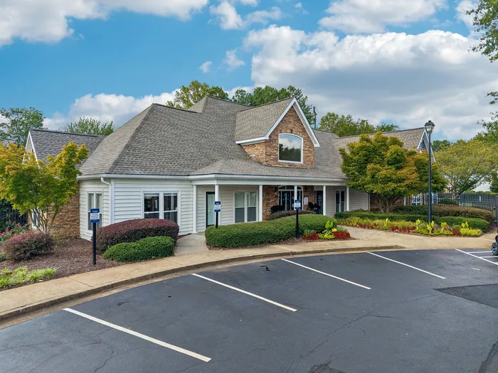 Charming apartment exterior showcasing a beautifully landscaped entrance, inviting architecture, and ample parking space under a vibrant sky.