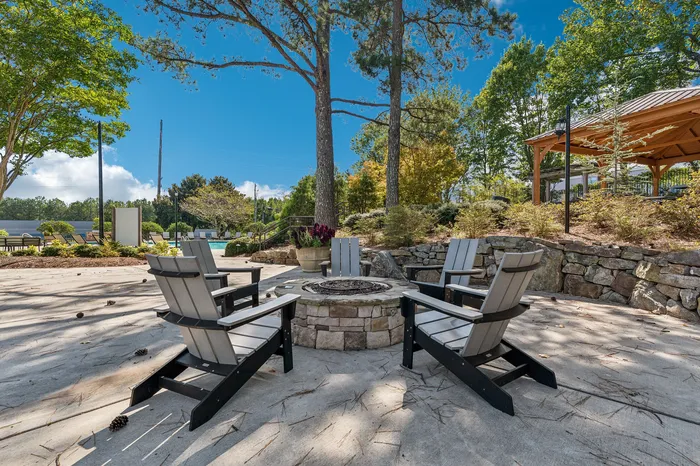 Charming outdoor patio with cozy seating surrounding a stone fire pit, nestled amidst lush greenery and mature trees, perfect for relaxing and entertaining.
