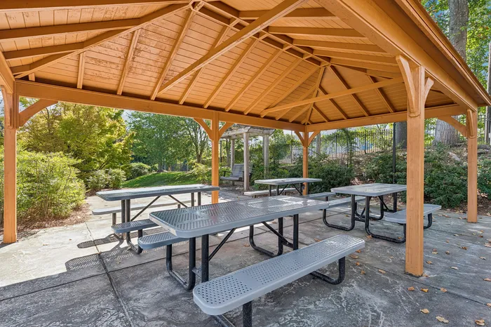 Charming outdoor gazebo with modern picnic tables, nestled in lush greenery, ideal for relaxing and social gatherings.