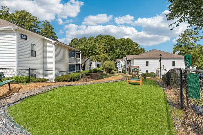 Charming apartment complex with manicured lawns, surrounded by lush greenery and bright blue skies, offering serene living.