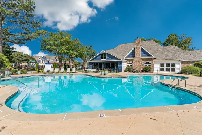 Inviting residential swimming pool with sun loungers and elegant clubhouse under a clear blue sky.