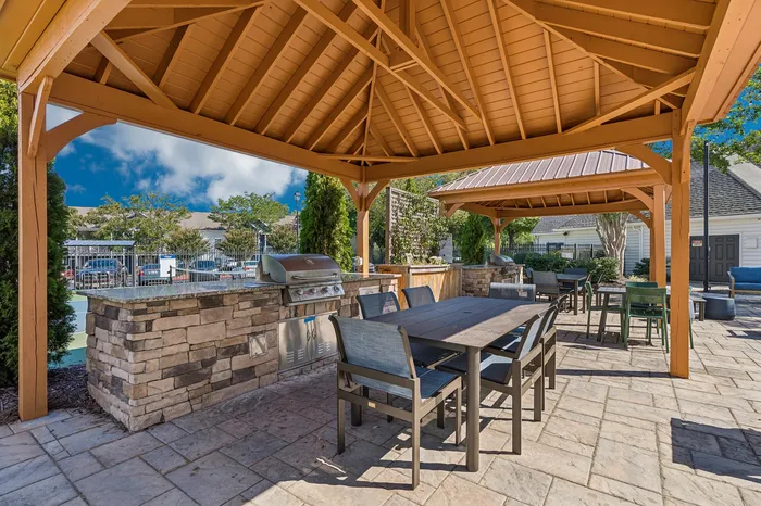 Inviting outdoor patio area featuring a stylish pergola with modern dining set, perfect for entertaining guests with a built-in BBQ grill under a sunny sky.