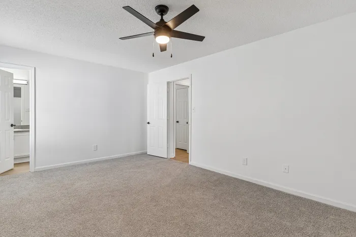 Spacious bedroom with plush carpet, sleek ceiling fan, and direct access to bathroom, exuding modern elegance.