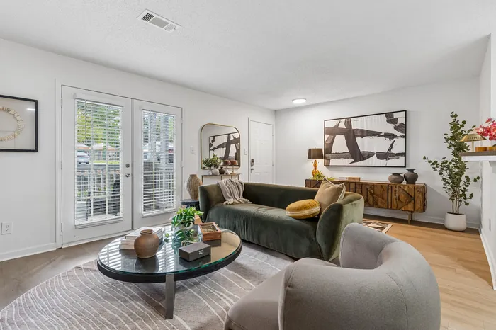 Chic living room with a plush green sofa, elegant coffee table, and stylish decor, bathed in natural light through a set of French doors.